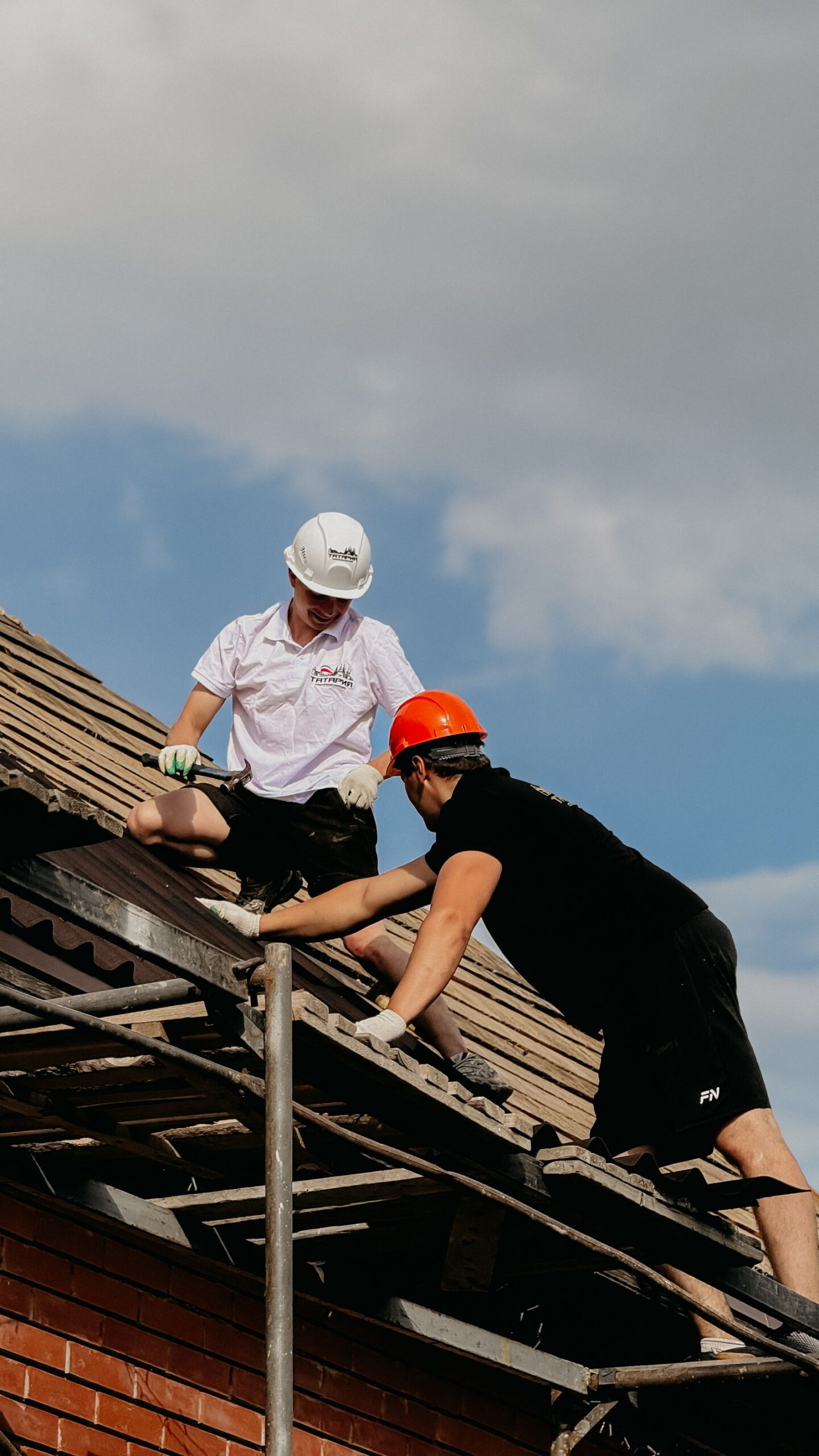 Two workers in helmets repairing a roof